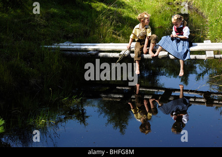 Jungen und Mädchen in traditioneller Kleidung, sitzen auf einem hölzernen Steg am See, Alp, Südtirol, Italien Stockfoto