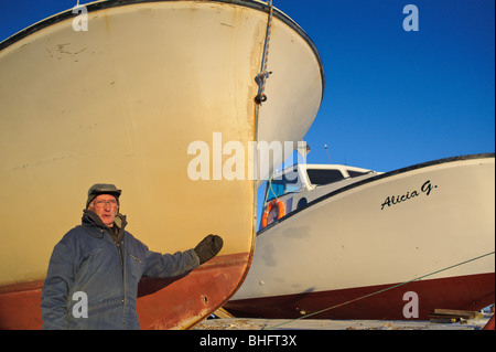 Alter Fischer gekleidet in Winterkleidung an gefrorenen Miramichi Bucht mit Kappe in New Brunswick, Kanada Stockfoto