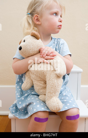Mädchen mit Teddybär und Putze auf Knien Stockfoto