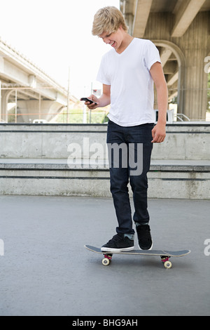 Teenager auf Skateboard mit Handy Stockfoto