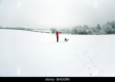 Lady wirft eine Spielzeug für ihren Hund Labradoodle, während in der Mitte ein Feld, das mit Schnee bedeckt ist Stockfoto