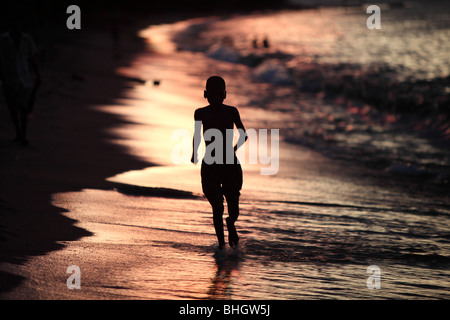 Ein Junge läuft am Strand entlang am Ufer des Lake Malawi mit Silhouette sichtbar. Im Dorf Chembe, Cape Maclear, Malawi Stockfoto