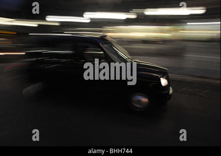 Klassisches Londoner Taxi in Schwarz bei Nacht mit Bewegungsunschärfe, um Geschwindigkeit zu zeigen Stockfoto