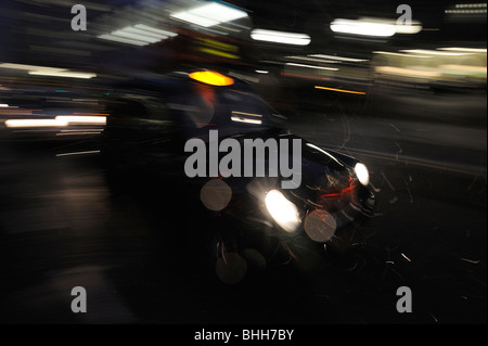 Klassisches Londoner Taxi in Schwarz bei Nacht mit Bewegungsunschärfe, um Geschwindigkeit zu zeigen Stockfoto