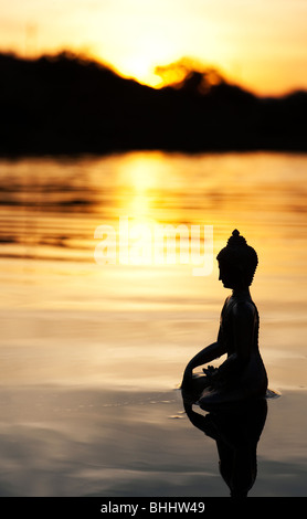 Silhouette der Buddha-Statue, die schwimmend auf ruhige Wasseroberfläche noch bei Sonnenaufgang in Indien Stockfoto