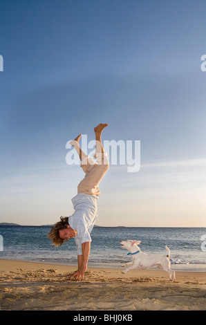 Mann steht auf Händen am Strand mit Hund Stockfoto