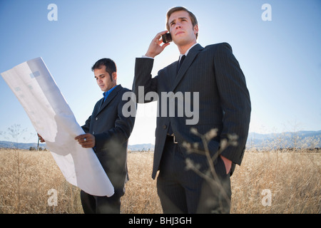 2 Männer mit Plänen im Feld, auf Handy Stockfoto