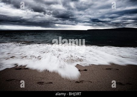 Wellen am Strand mit Fußspuren Stockfoto