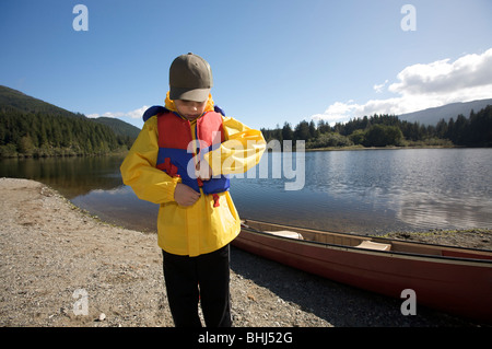 Ein kleiner Junge setzt auf ein PFD vor dem Schlafengehen auf einem Kanu Stockfoto