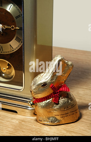 Ein Lindt-Goldfolie gewickelt Schokoladen Osterhase sitzt neben einer Uhr. Stockfoto