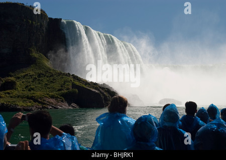 Touristen in blauen Regenmänteln und Horseshoe Falls, wie sie vom Touristenboot Maid of the Mist auf dem Niagara River aus gesehen werden, erleben den mächtigen Wasserfall Nebel. Stockfoto