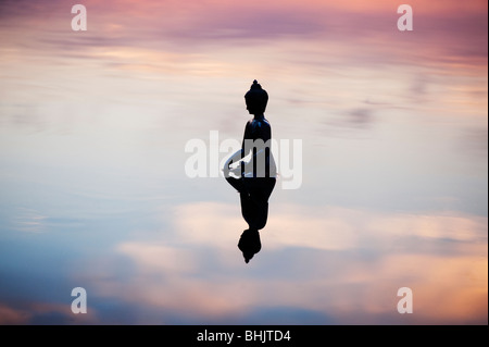 Silhouette der Buddha-Statue, die schwimmend auf ruhige Wasseroberfläche noch kurz vor Sonnenaufgang in Indien Stockfoto