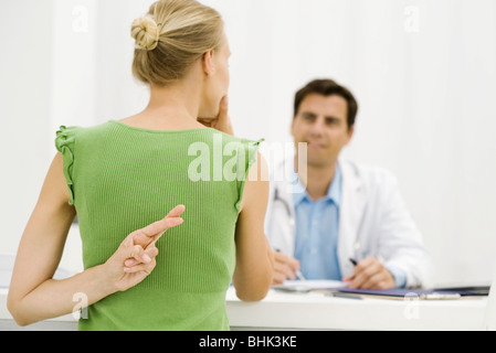 Patientin mit Hand hinter Finger, Rückkreuzung mit Arzt gesprochen Stockfoto