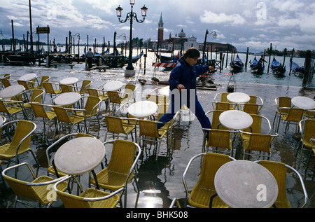 Venedig, Italien. Eine Mädchen springt zwischen Café Stühle zu vermeiden nass während der Flut, Acqua Alta, San Marco. Stockfoto