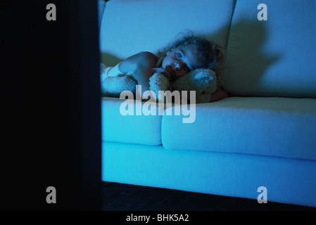Mädchen auf Sofa liegend mit Teddybär, vor dem Fernseher Stockfoto