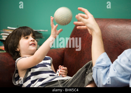 Kleiner Junge werfen Kugel mit übergeordneten auf sofa Stockfoto