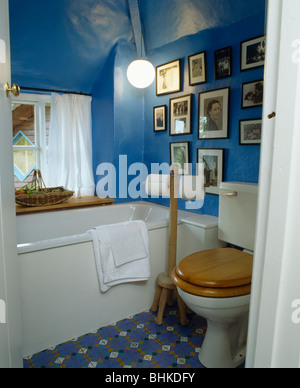 Schwarz + weiß Fotosammlung an Wand in kleinen blauen Dachgeschoss Bad mit Holzsitz auf Toilette Stockfoto