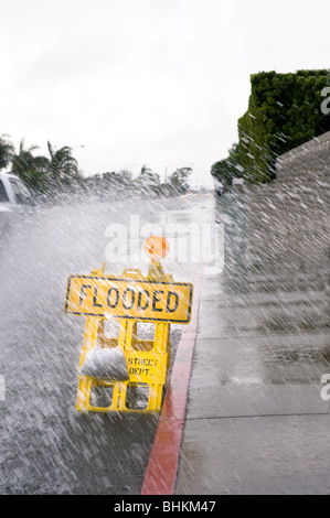 Ein Auto tritt ein Pool von Regenwasser über ein Straßenschild überflutet bei schlechtem, regnerischem Wetter. Stockfoto