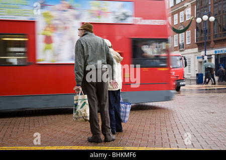 Ältere Fußgänger warten auf einen Bus vor dem Überqueren der Straße im Regen, Kingston, Surrey, England übergeben. Stockfoto