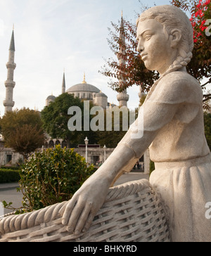 Die blaue Moschee, Istanbul, Türkei bietet eine Kulisse für eine Statue von einer jungen Frau hält einen Korb ich Stockfoto