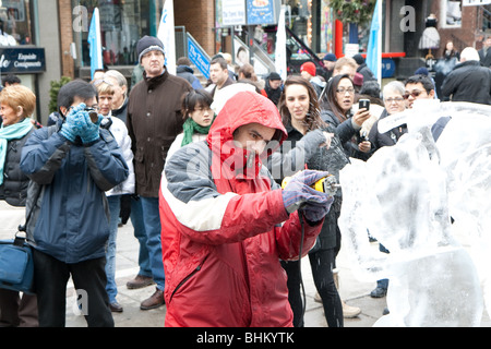 Ein Ice Carving-Künstler arbeitet an seine Eisskulptur, während das Publikum auf der Straße sehen Sie auf Stockfoto