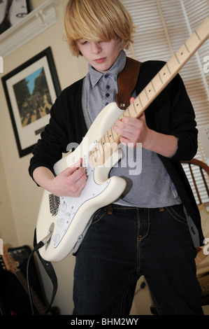 Teenager junge Gitarrist spielt eine Creme Fender Stratocaster in seinem Wohnzimmer mit The Beatles-Abbey Road Album an der Wand. Stockfoto