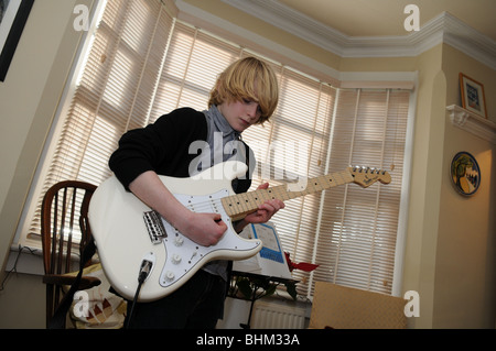 Teenager-Jungen üben den Blues in seinem Wohnzimmer auf einer Creme Fender Stratocaster-Gitarre, umrahmt von einem Erker als Kulisse Stockfoto