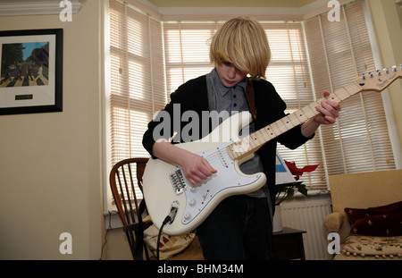 Teenager-Jungen üben den Blues in seinem Wohnzimmer auf einer Creme Fender Stratocaster-Gitarre mit einem Beatles-Album an der Wand Stockfoto