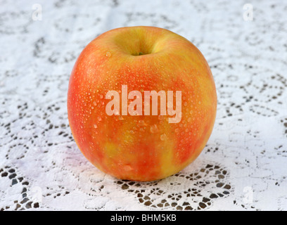 Frisch, reifer, Pink Lady Apfel mit Wasser tropft auf Spitze Tischdecke. Stockfoto