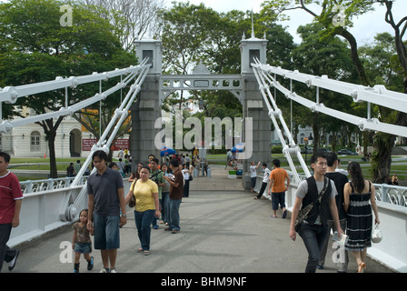 Fußgänger, die über die Cavenagh Bridge mit dem Esplanade Park im Hintergrund, Singapur, laufen Stockfoto