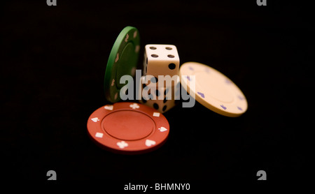zwei Würfel und drei Poker-Chips, die auf einer schwarzen Tischdecke platziert Stockfoto