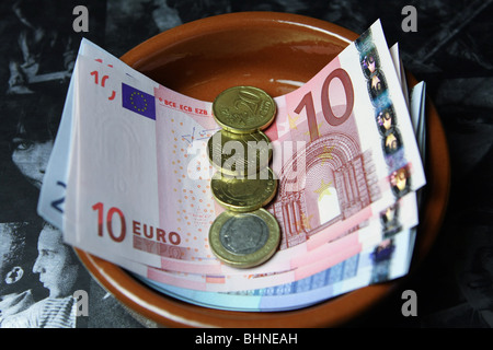 Euro-Banknoten und Münzen in einer Schale auf eine dunkle Seite eines aufgeschlagenen Buches Stockfoto