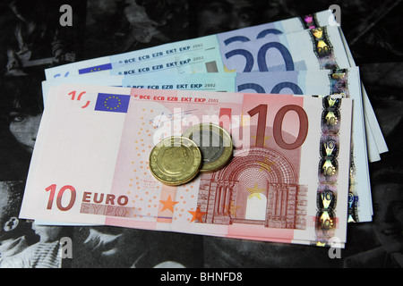 Euro-Banknoten und Münzen in einer Schale auf eine dunkle Seite eines aufgeschlagenen Buches Stockfoto