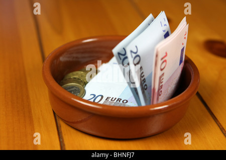 Euro-Banknoten und Münzen in einer Schale auf einer Holzoberfläche Stockfoto