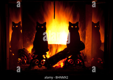 Leuchtend gelb und orange Flammen hinter silhouetted schwarze Katze Schmiedeeisen Feuerbocke in der gemütlichen warmen Kamin. Flammen leuchten durch die Augen der Katzen Stockfoto