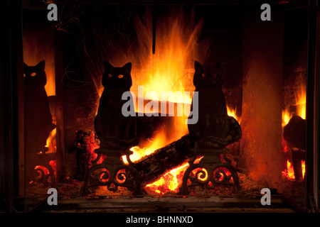 Leuchtend gelb und orange Feuer hinter silhouetted schwarze Katze Gusseisen Feuerbocke in gemütliche Kamin, Feuer leuchtet durch die Augen der Katze zahlen Stockfoto