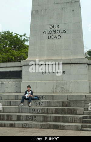 Ein Mann neben dem Ehrenmal Weltkrieg ein Denkmal sitzend, Esplanade Park, Connaught Drive, Singapur Stockfoto