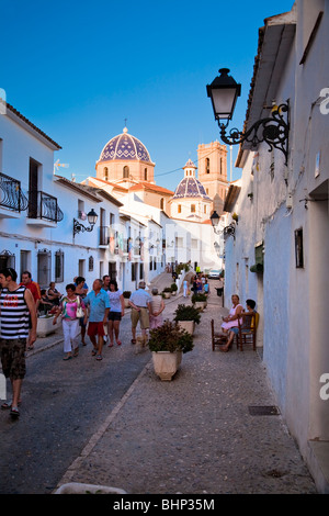 Menschen auf Straße, [Calle San Miguel] Altea, Alicante, Spanien. Mit Kirche "Virgen del Consuelo" im Hintergrund Stockfoto