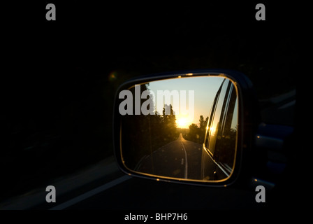 ein Heckflügel Spiegel zeigt die Ansicht der Landschaft vorbei Straße bei Sonnenuntergang verschwinden hinter Auto bewegen Stockfoto