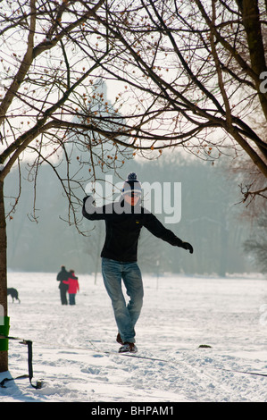 Guy, balancieren auf einem Seil im Schnee bedeckt englischen Garten mit der Bayerischen Staatskanzlei im Hintergrund zu sehen Stockfoto