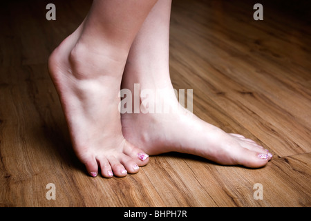 Die eleganten und edlen Füße einer Frau stehen im Mittelpunkt der natürlichen Wärme eines Holzfußbodens und zeigen die Kunstfertigkeit des Nageldesigns Stockfoto