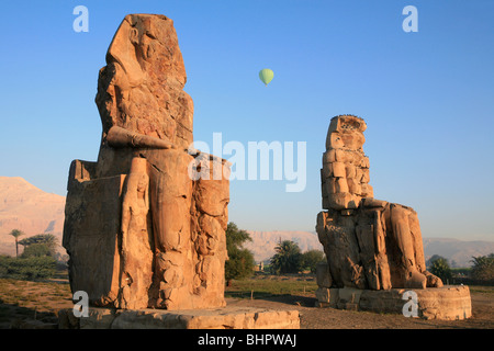 Eine grüne Heißluftballon überfliegen die Kolosse von Memnon bei Sonnenaufgang in der Nähe von Luxor, Ägypten Stockfoto