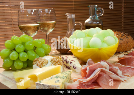 Eine Platte mit mediterranen Speisen wie Käse, Trauben, Wein, Brot, Parmaschinken, Melone, Olivenöl und Balsamico-Essig. Stockfoto