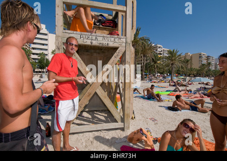 Junge Menschen zusammen entspannen auf den Strand von El Arenal Mallorca mit im Hintergrund Palmen und Hotels Stockfoto