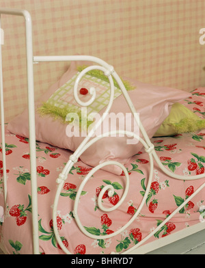 Nahaufnahme des weißen Schmiedeeisen-Bett mit blass rosa Kissen und Erdbeere-Print Bettwäsche Stockfoto