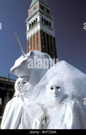 Paar in weißen Kostümen, mit Einhorn Hut, andere halten Calla Lily, San Marco Campanile hinter, Karneval in Venedig, Italien Stockfoto