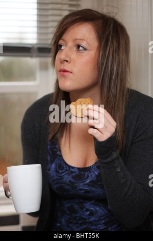 Eine junge Frau einen verdauungsfördernden Keks essen und trinken ein heißes Getränk. Stockfoto