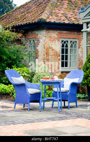 Helle blaue Lloyd Loom-Sessel und Tisch auf gepflasterten Terrasse vor traditionelle Country house Stockfoto