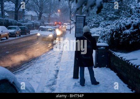 Als blaue Dämmerung, die Licht erhellt erwartet zu einem anderen winterlichen Tag in Süd-London ein Pendler die Ankunft von einem weit entfernten roten Bus. Stockfoto