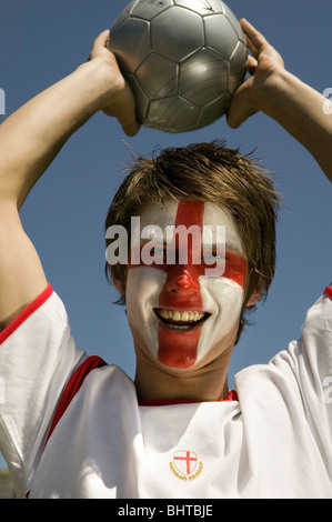 eine jubelnde England Fußball-Anhänger mit der St. Georgs-Flagge gemalt auf seinem Gesicht halten einen Fußball Stockfoto